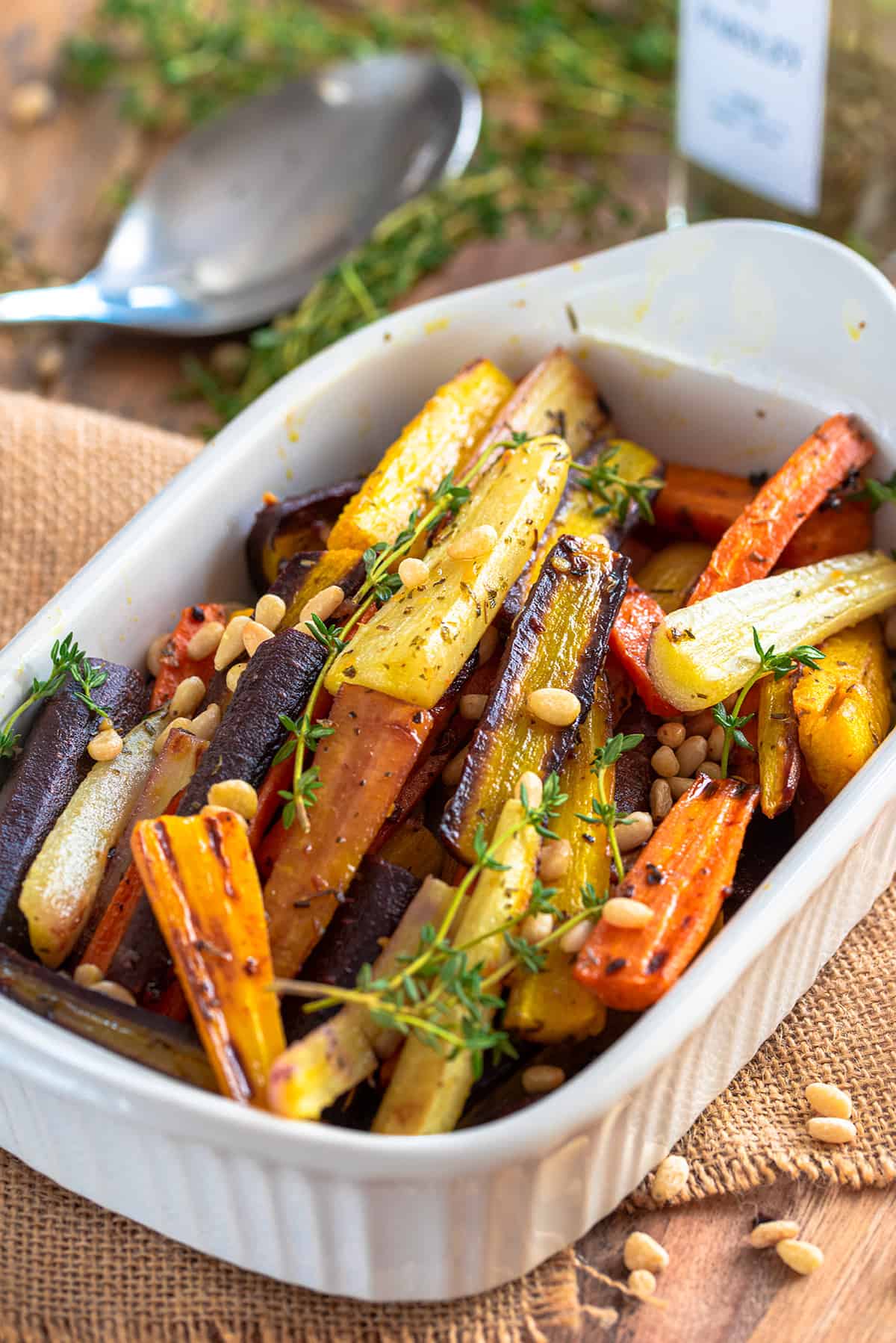 Roasted carrots in a white serving dish with fresh thyme and pine nuts sprinkled over top.