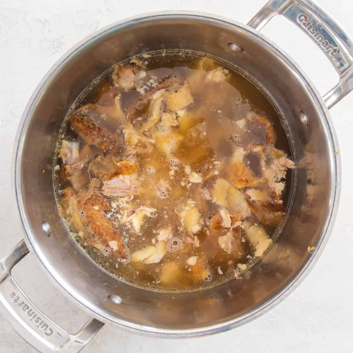 Looking down into a stockpot of chicken stock and chicken pieces.