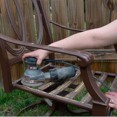 Woman sanding a metal chair with an orbital sander.