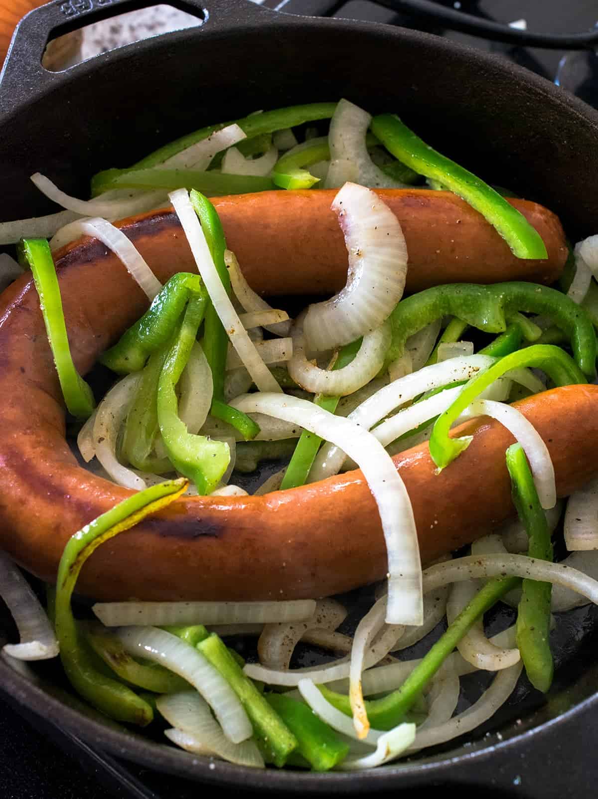 Cast iron skillet with whole kielbasa sausage and slice onions and green peppers.