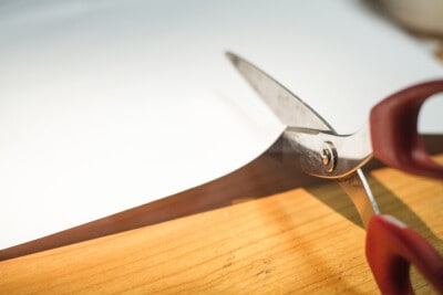 A pair of scissors cutting a sheet of paper for a template.