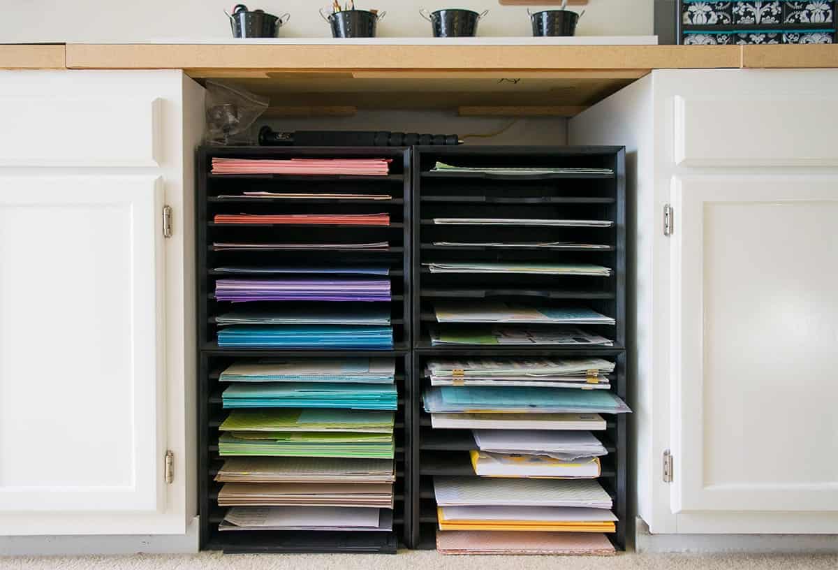 White cabinets in craft office with paper sorters stacked under the countertop and rainbow color coded cardstock.