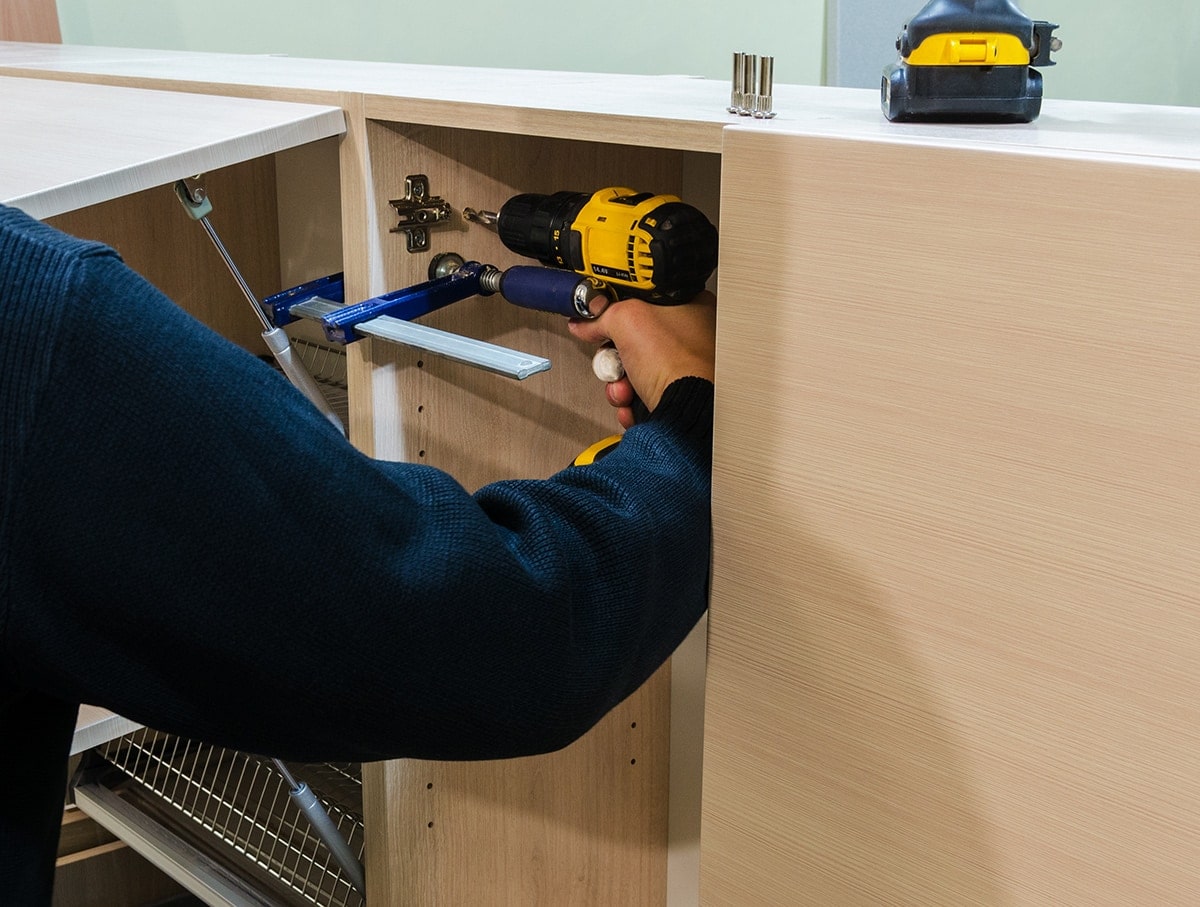 Man using a drill and clamps to attach wall cabinets together.