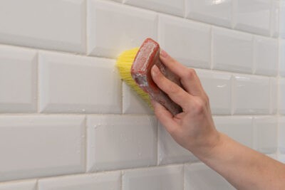 Closeup of a hand scrubbing a tile wall.