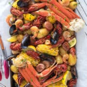 Seafood boil overhead on a table with crab legs, mussels, crawfish, potatoes, corn, and cajun butter sauce.