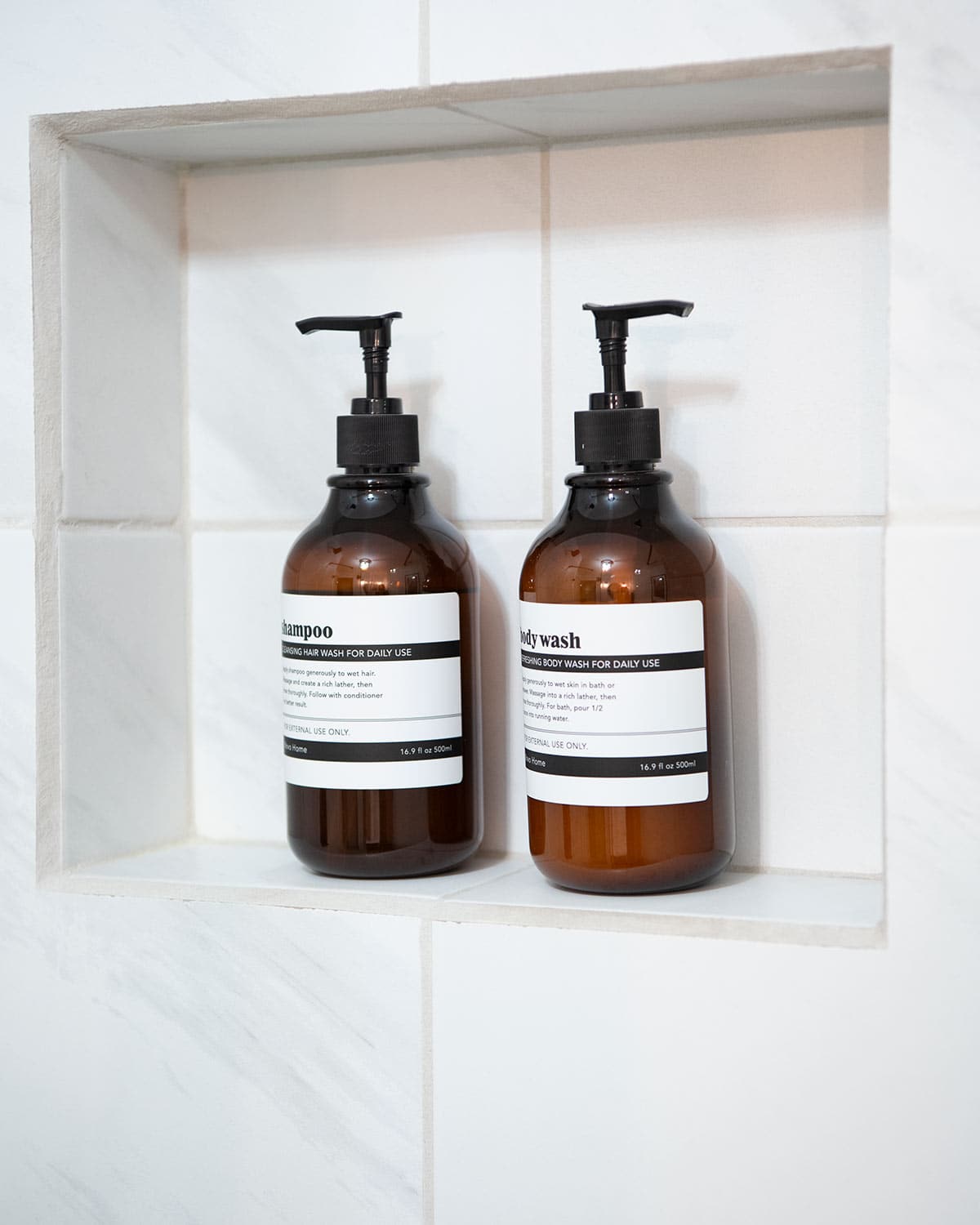 Two bottles of shampoo and body wash in a simple white shower niche.