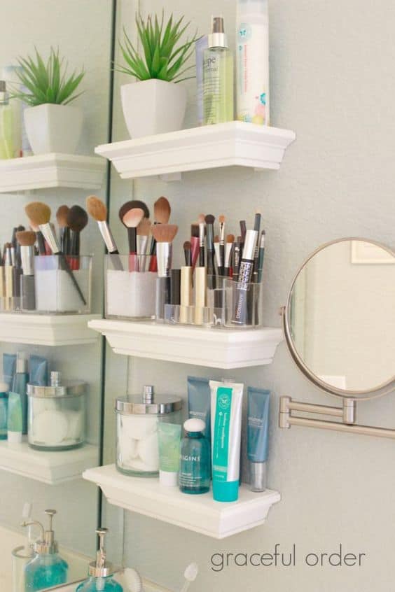 White floating shelves on bathroom wall used for storing makeup brushes, toiletries, and small potted plant.