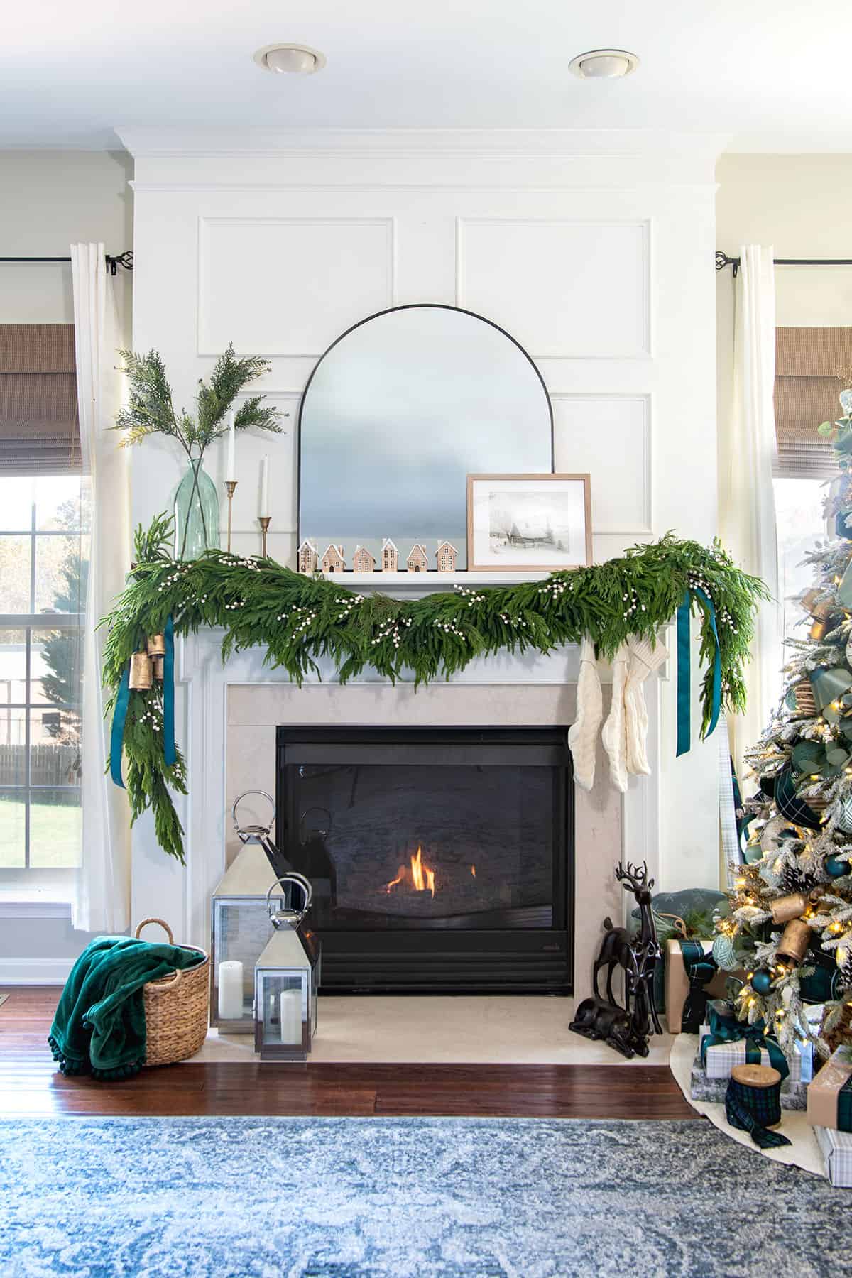 A fireplace mantel decorated for Christmas with garland, mirror, greenery, and candles.