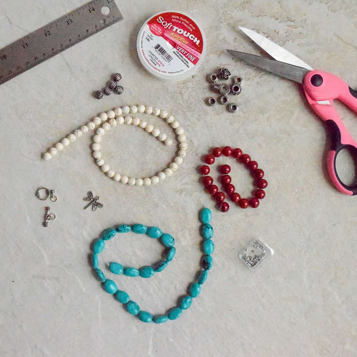 Supplies for making a simple DIY beaded bracelet- beads, scissors, charms, ruler, and elastic string.