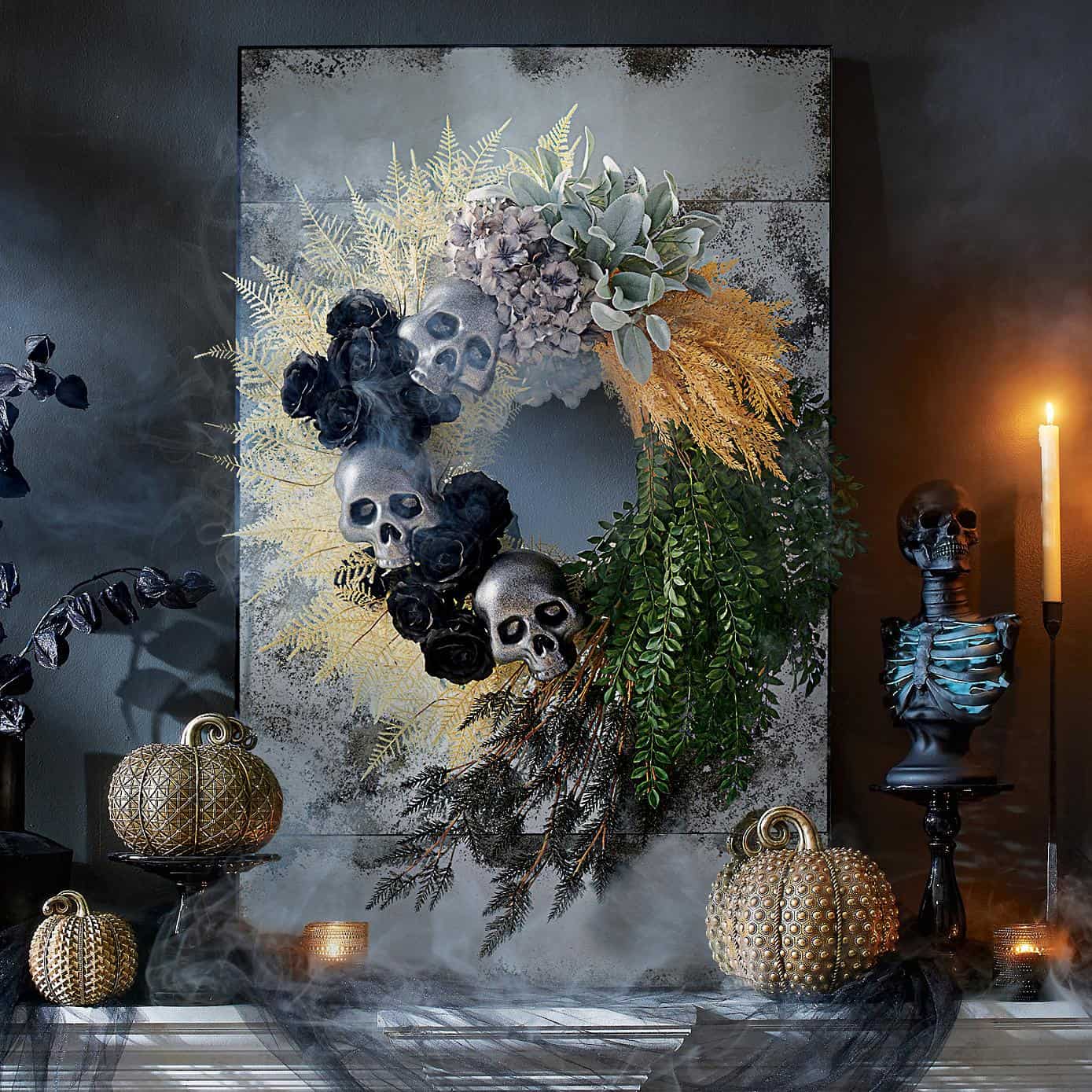 Spooky skull wreath flanked by skeleton bust and metallic textured pumpkins lit by candlelight.
