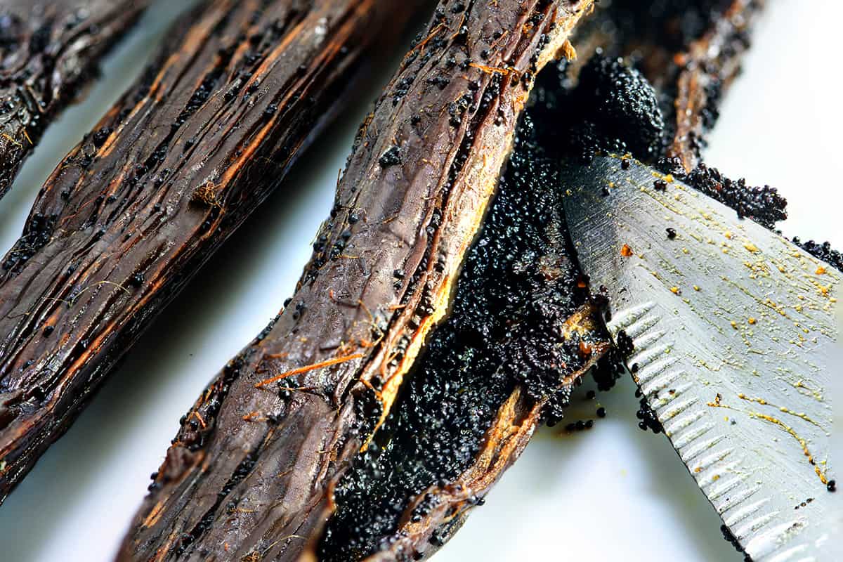Closeup of knife splitting a vanilla bean open to show the inside.