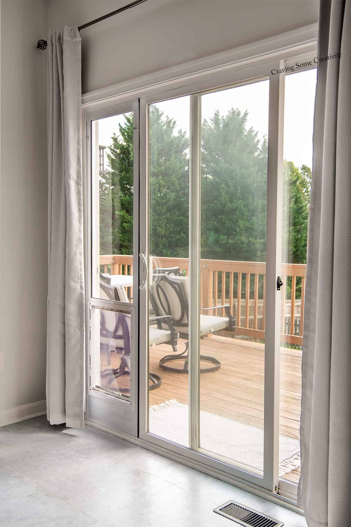 Glass patio doors with a dog door inserted into the frame and a view of the back deck including railing.