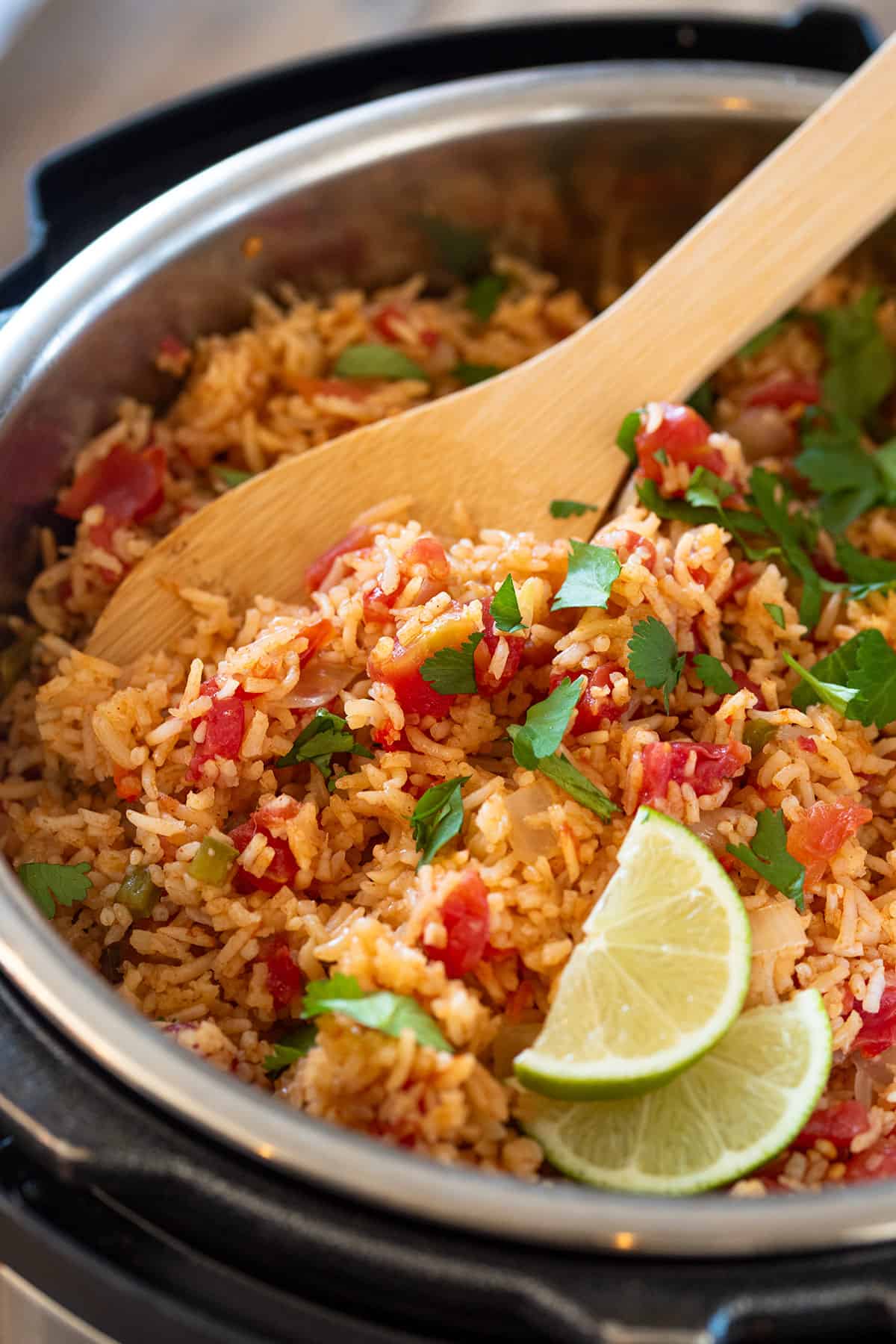 Mexican rice garnished with lime slices and cilantro in a slow cooker with spoon to fluff the rice.