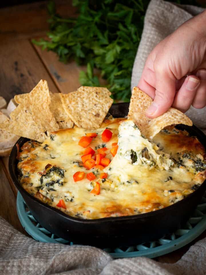 Cheese pull of spinach artichoke dip with hand dipping a tortilla chip.