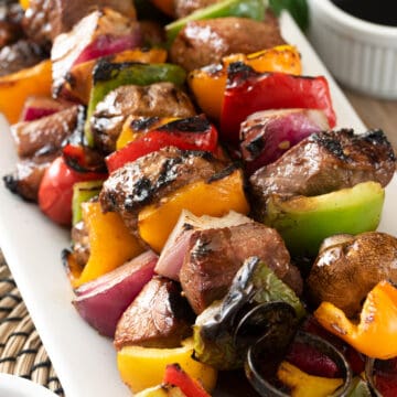 Steak kabobs skewered on a plate.