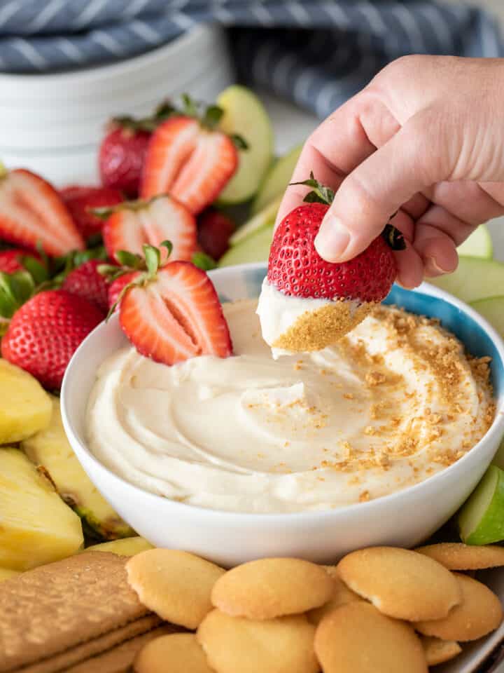 Woman dipping a strawberry into cheesecake dip with graham crackers on top.