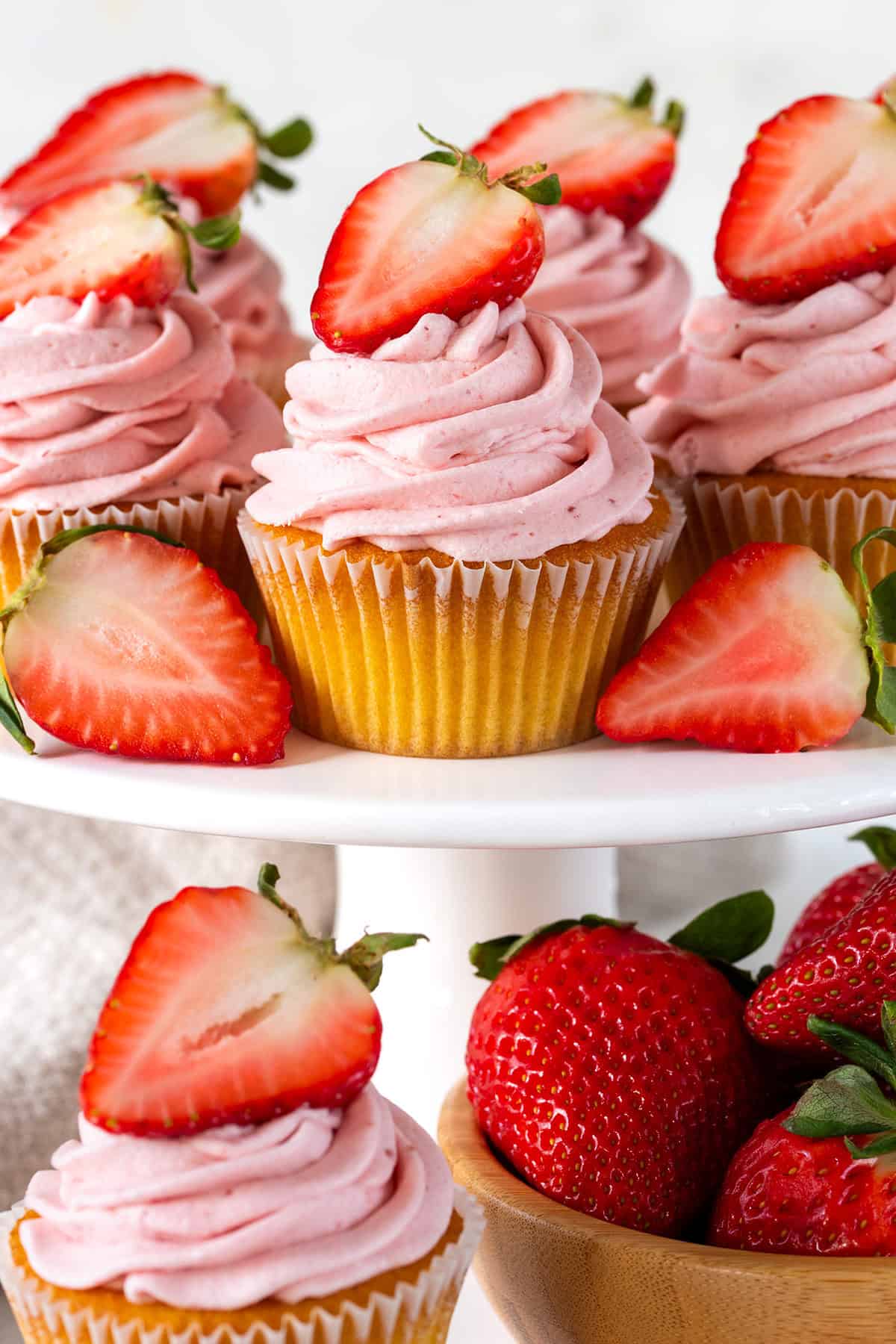 Close up of cupcake tier featuring Strawberry Cream Cheese Frosted cupcakes with fresh strawberries sliced and whole.