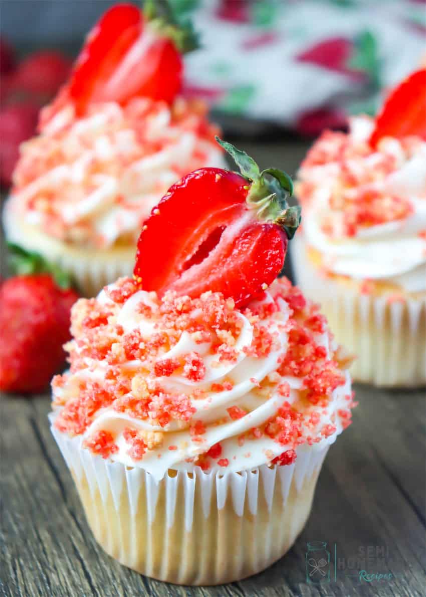 Strawberry crunch cupcakes with white frosting and a sliced strawberry on top.