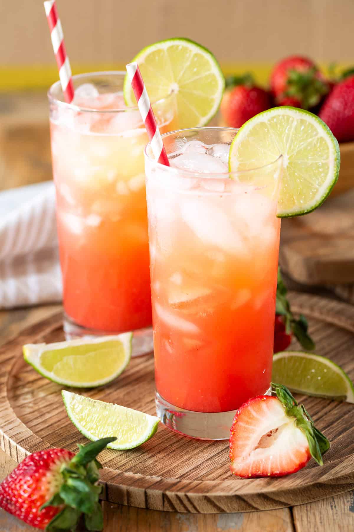 Two glasses of strawberry limeade with lime garnish on a wood background.
