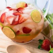 Pitcher of strawberry sangria on a table with wood spoon in front.