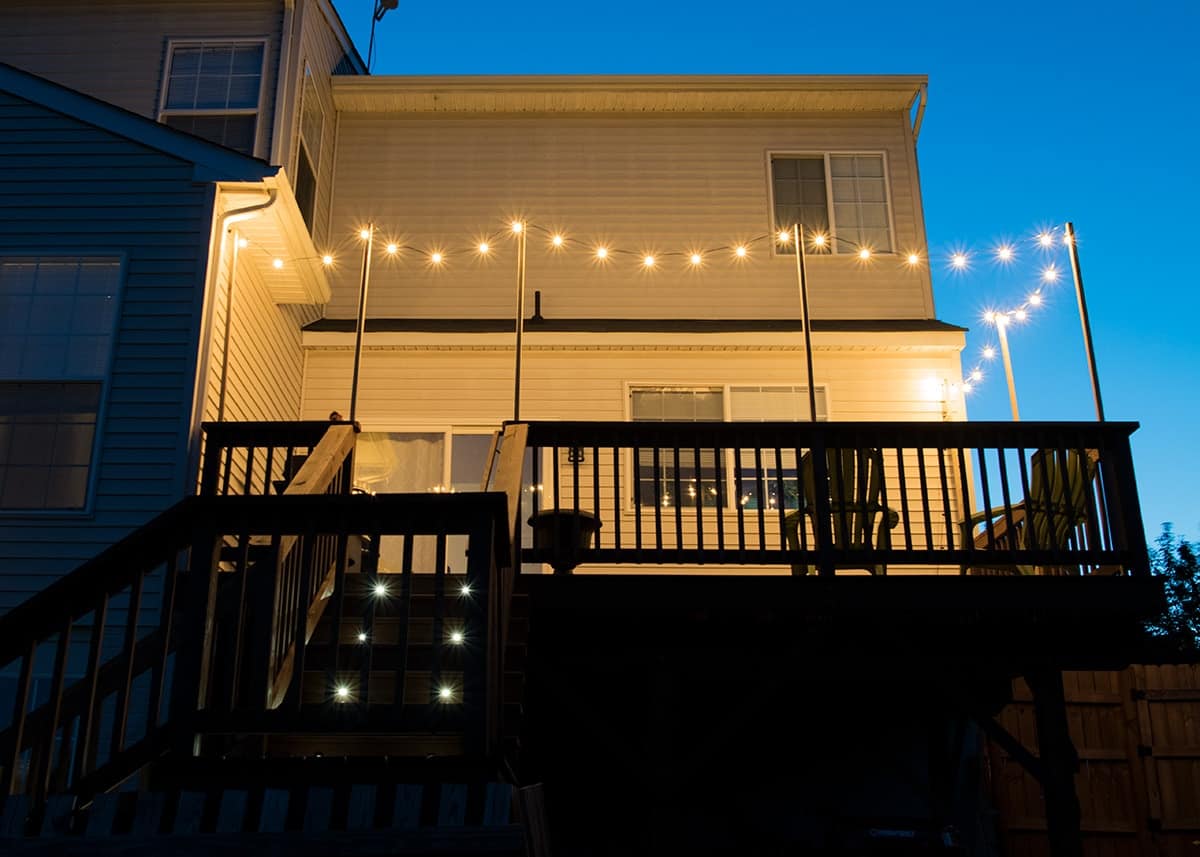 Raised wooden deck with hanging string lights at night so they glow.