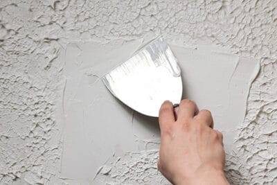 Smoothing out texture on a ceiling with a putty scraper.