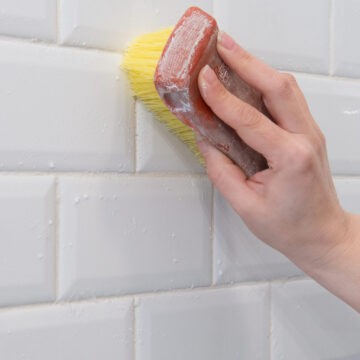 Closeup of a woman cleaning white tile grout.