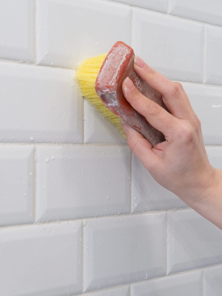 Closeup of a woman cleaning white tile grout.