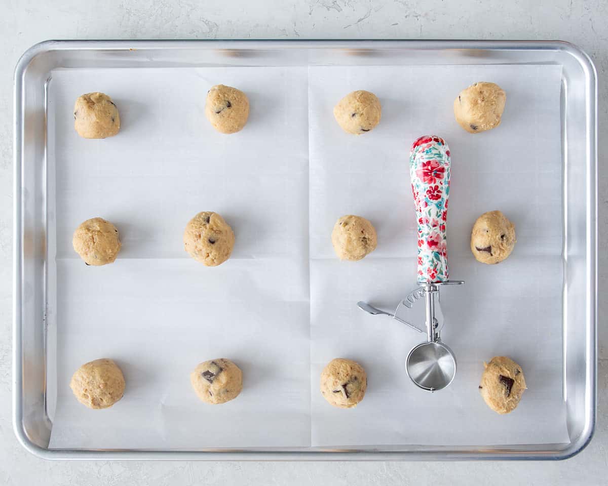 A sheet pan with rolled cookie balls and a #40 cookie scoop on it.