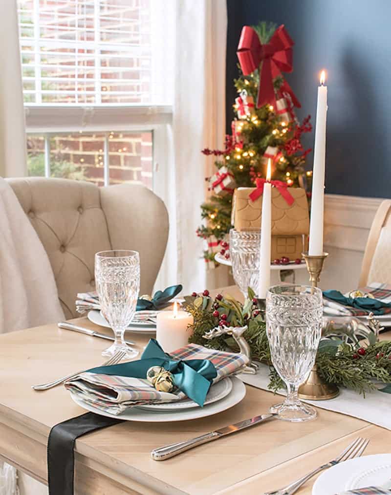 Modern traditional Christmas dining room with Christmas plaid, goblets, a gingerbread house, and a small lighted Christmas tree in a corner.