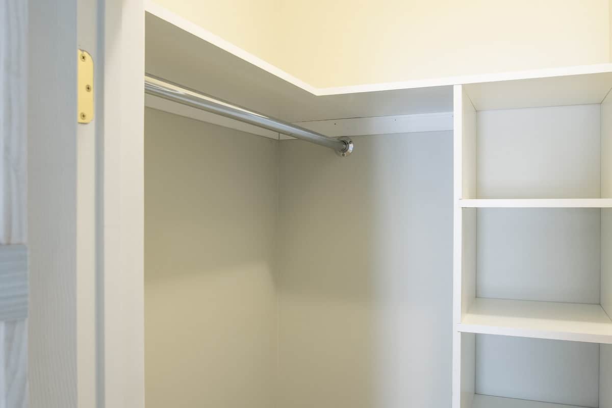 Custom built white shelving in walk-in closet with metal bar for hanging clothes.