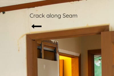 Cracked drywall seam above a door frame where two sheets of drywall create a seam.