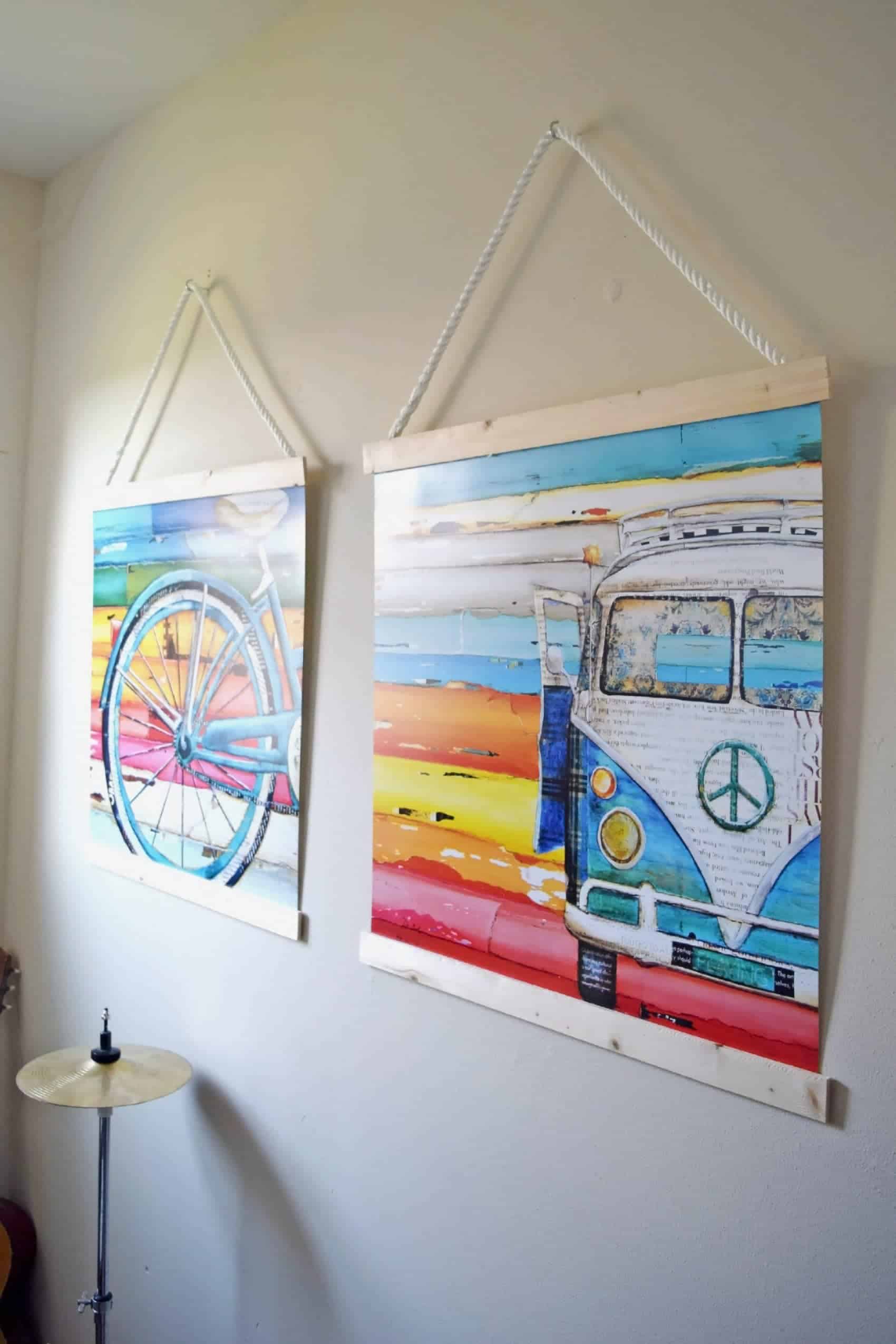 DIY wooden frames on white hanging ropes with colorful bicycle and VW bus art on white wall.
