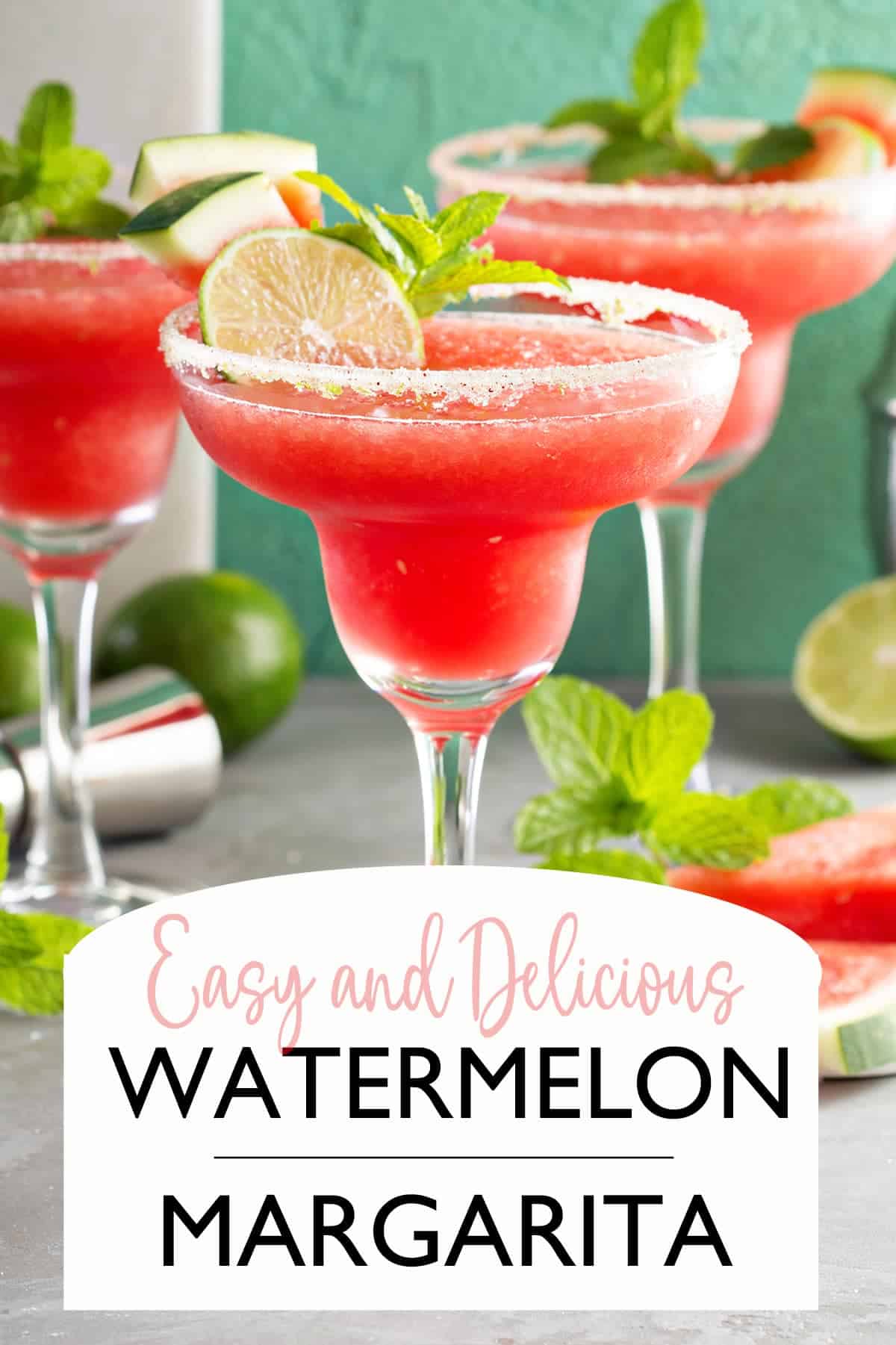 Frozen Watermelon margaritas with sugar rim, mint, limes and slices of watermelon in background.