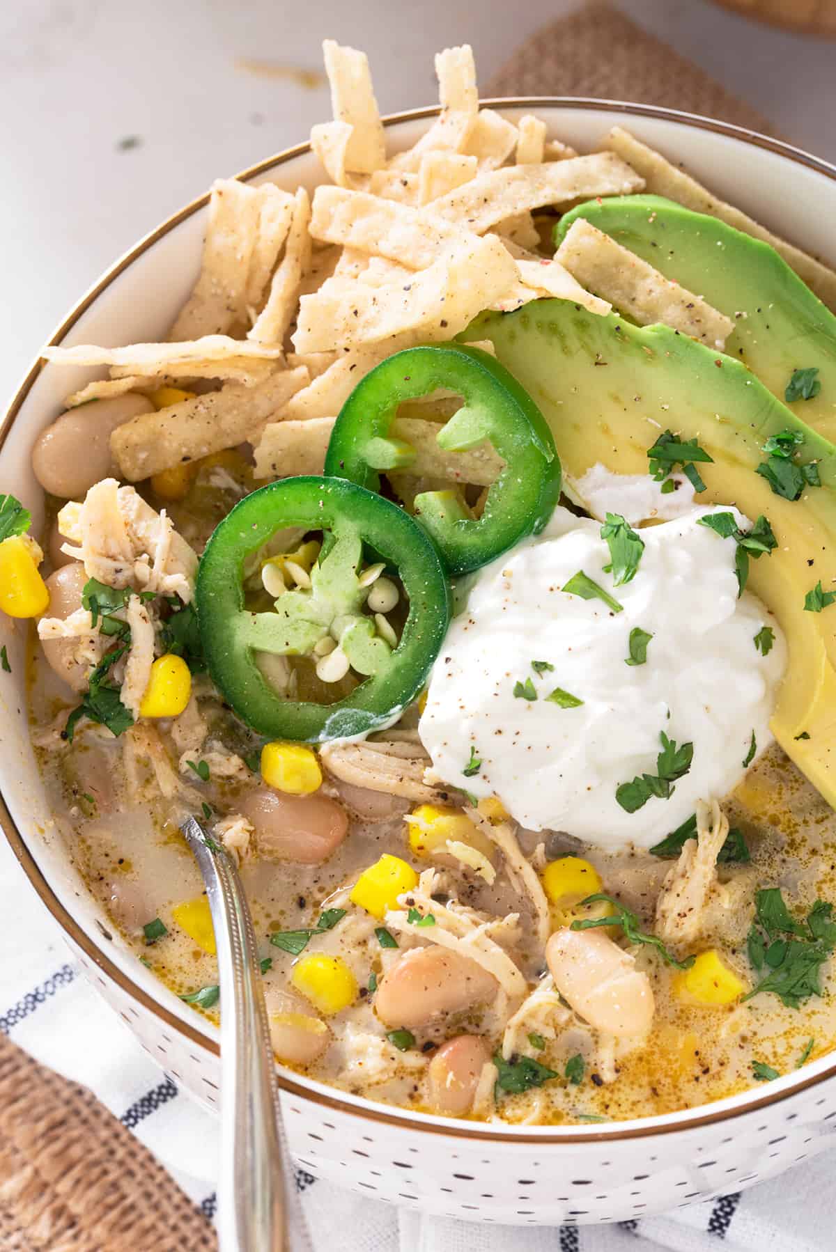 Top down view of a bowl of white chicken chili garnished with avocado, sour cream, jalapeno, and tortilla strips.