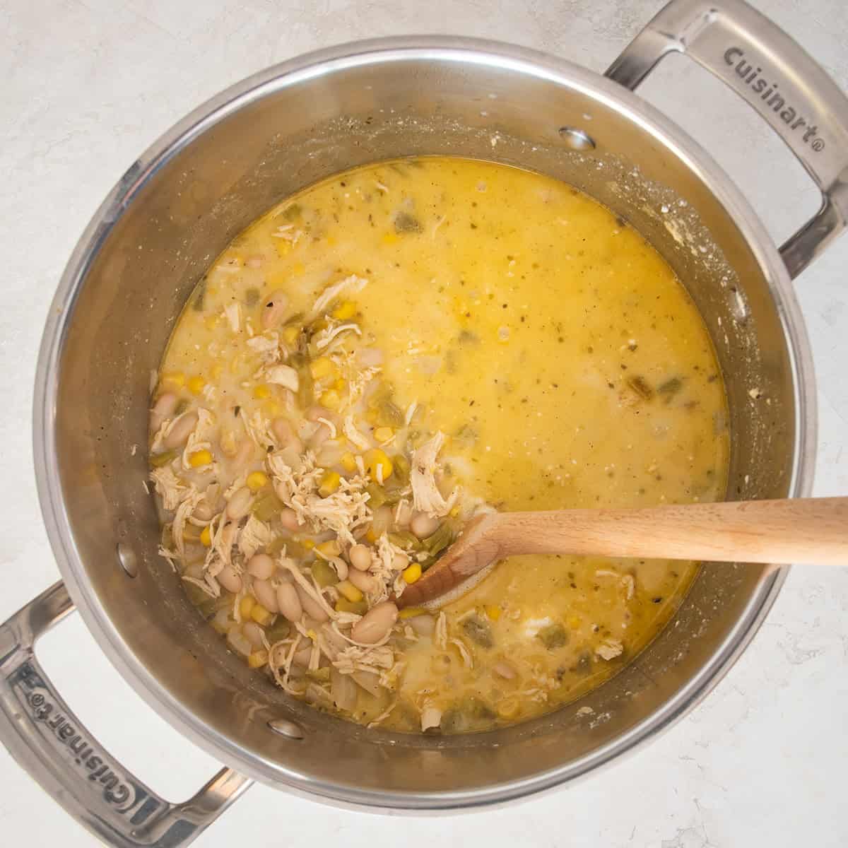 Top down view into white chicken chili as the white cream and cream cheese are put in and stirred.