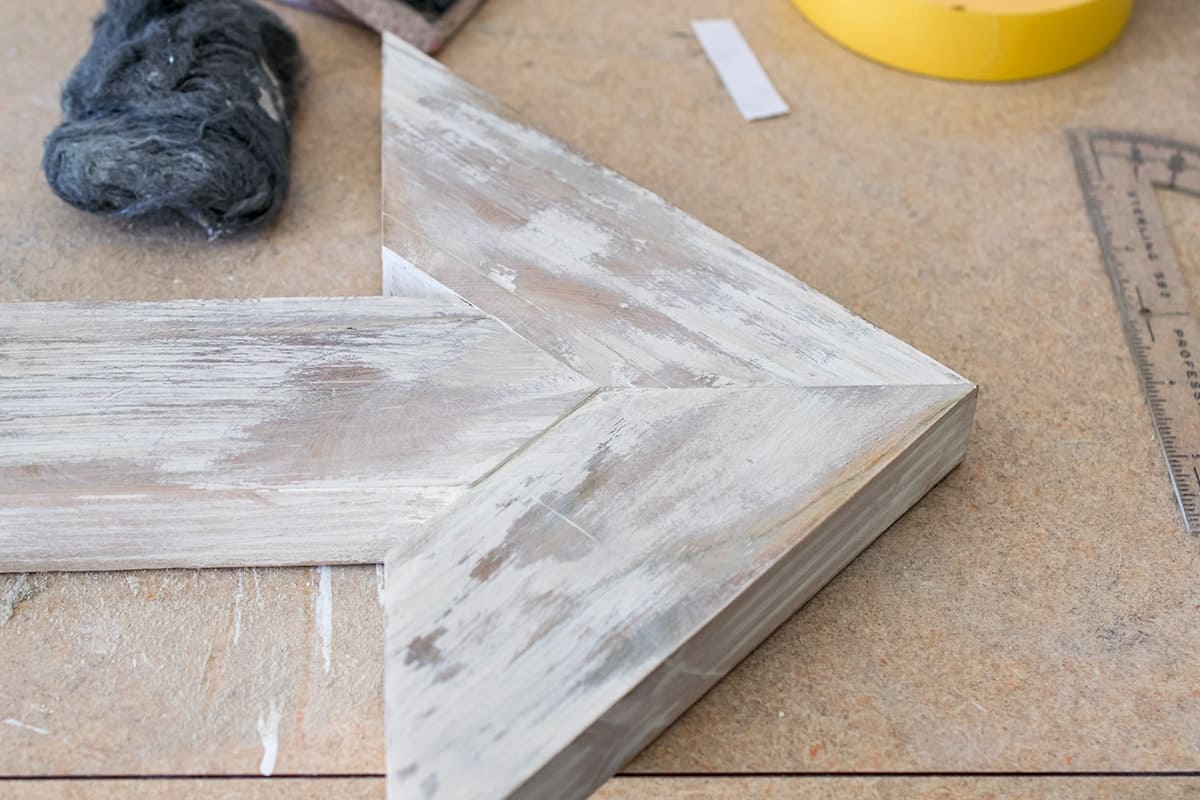 Whitewash finish on DIY wooden arrow point laying on work bench next to tools.