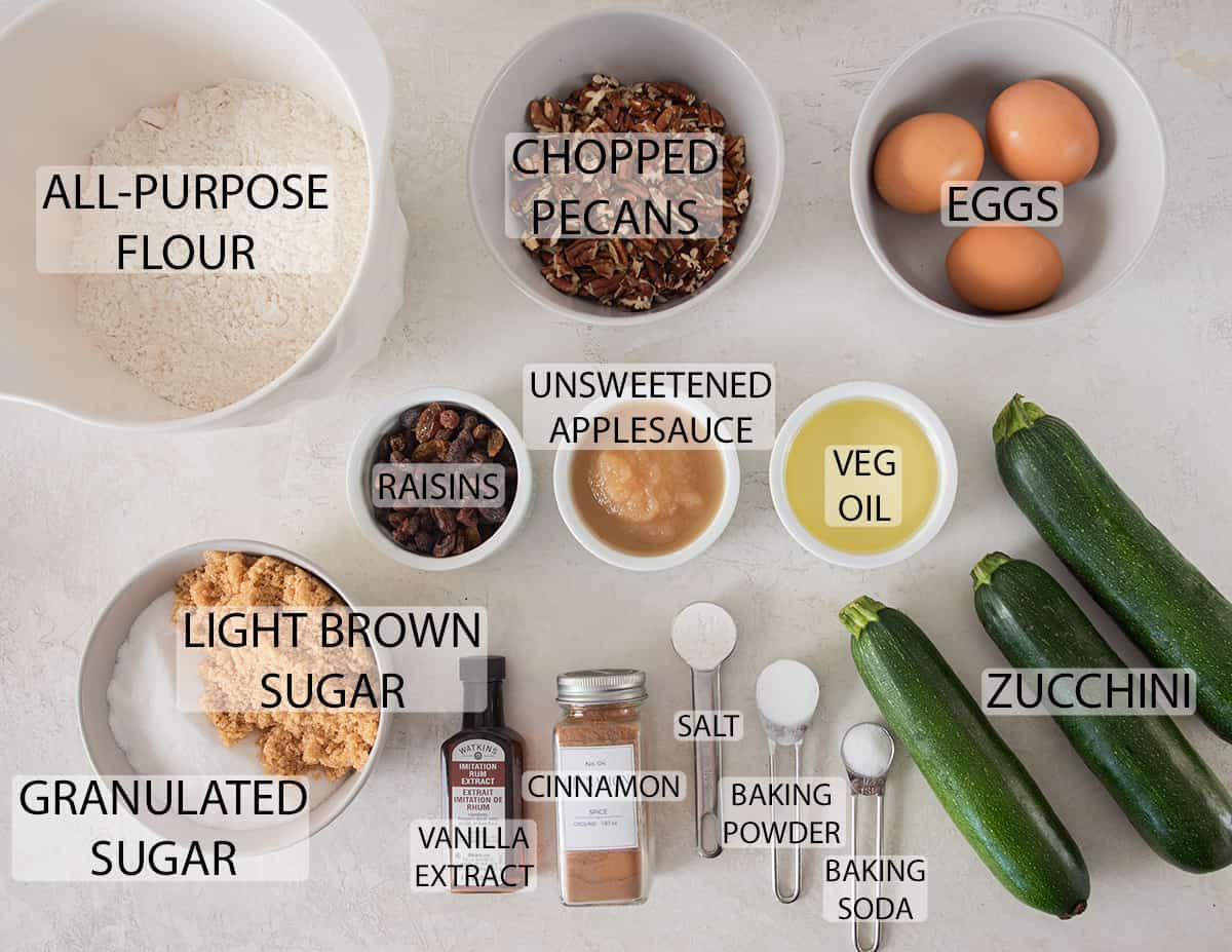 Ingredients to make zucchini muffins with raisins and pecans with text labels.