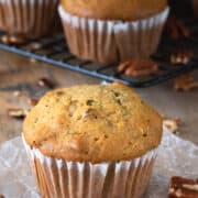 Zucchini Muffin in a paper wrapper with several muffins in the background.