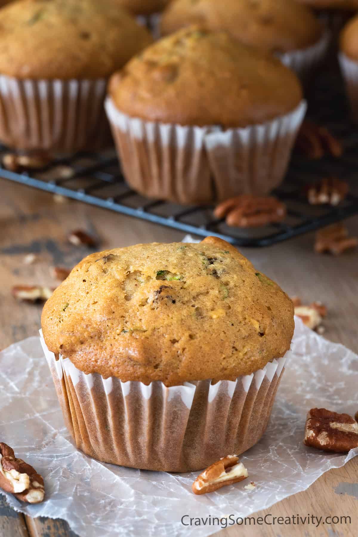 Zucchini muffin in wrapper centered on wood background with several other muffins in the background.