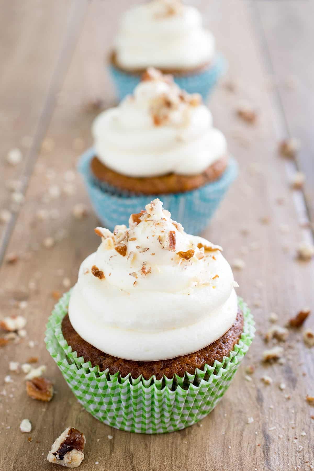 Three cupcakes with homemade cream cheese frosting and sprinkled with nuts.